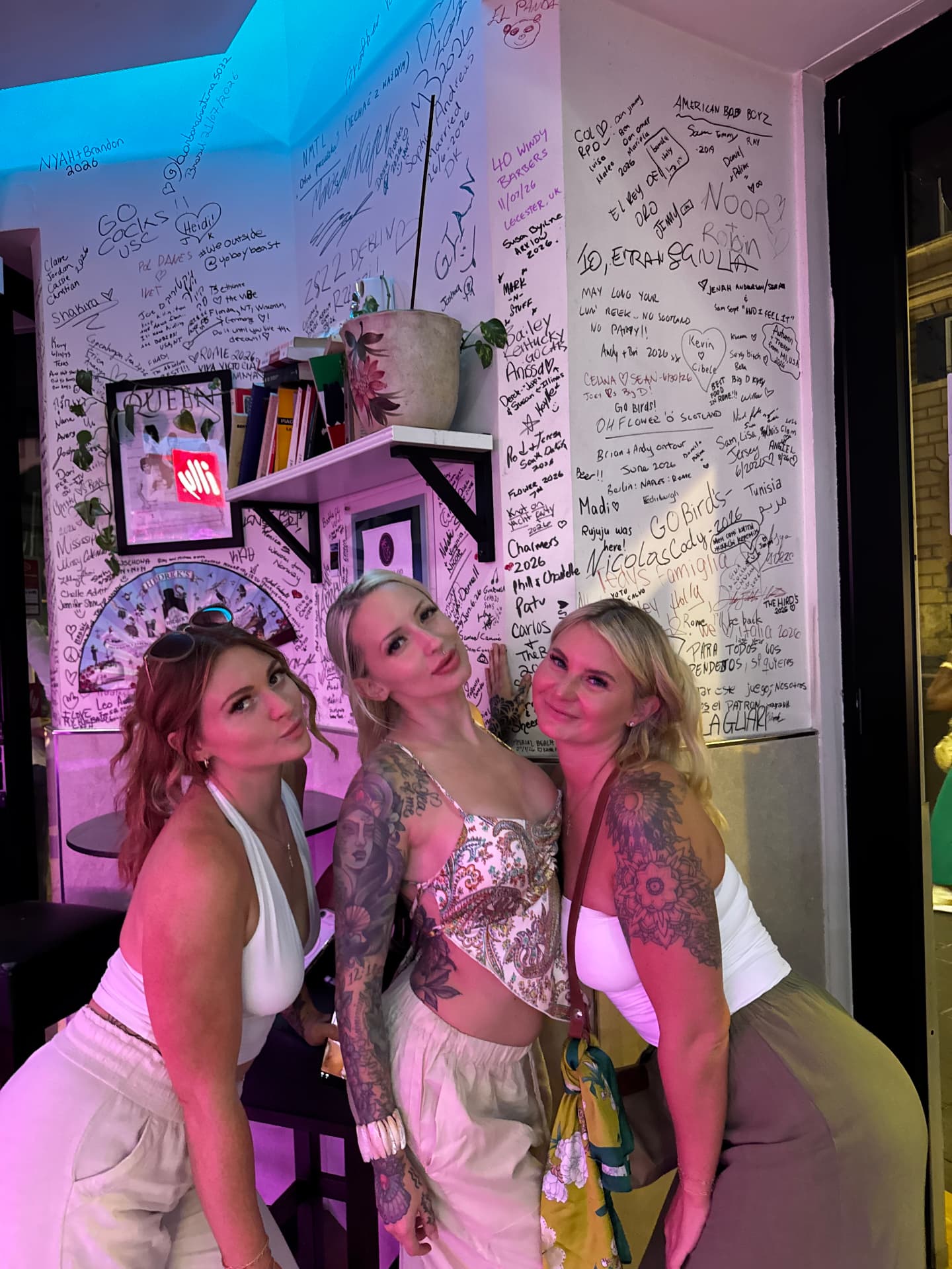 Three friends posing in front of the signature-covered wall at Miami Pub Roma