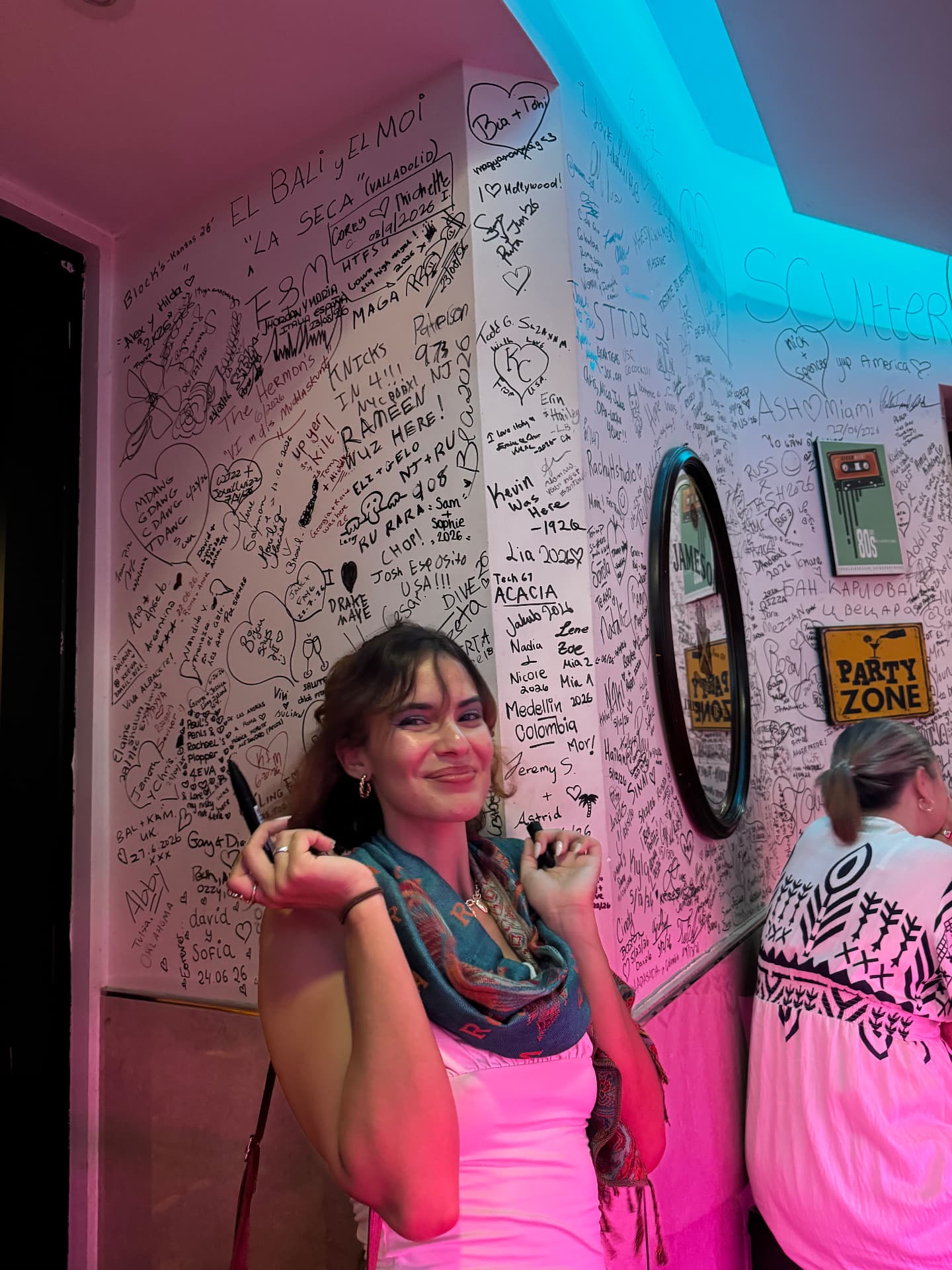 A guest holding a marker in front of the signed wall at Miami Pub Roma